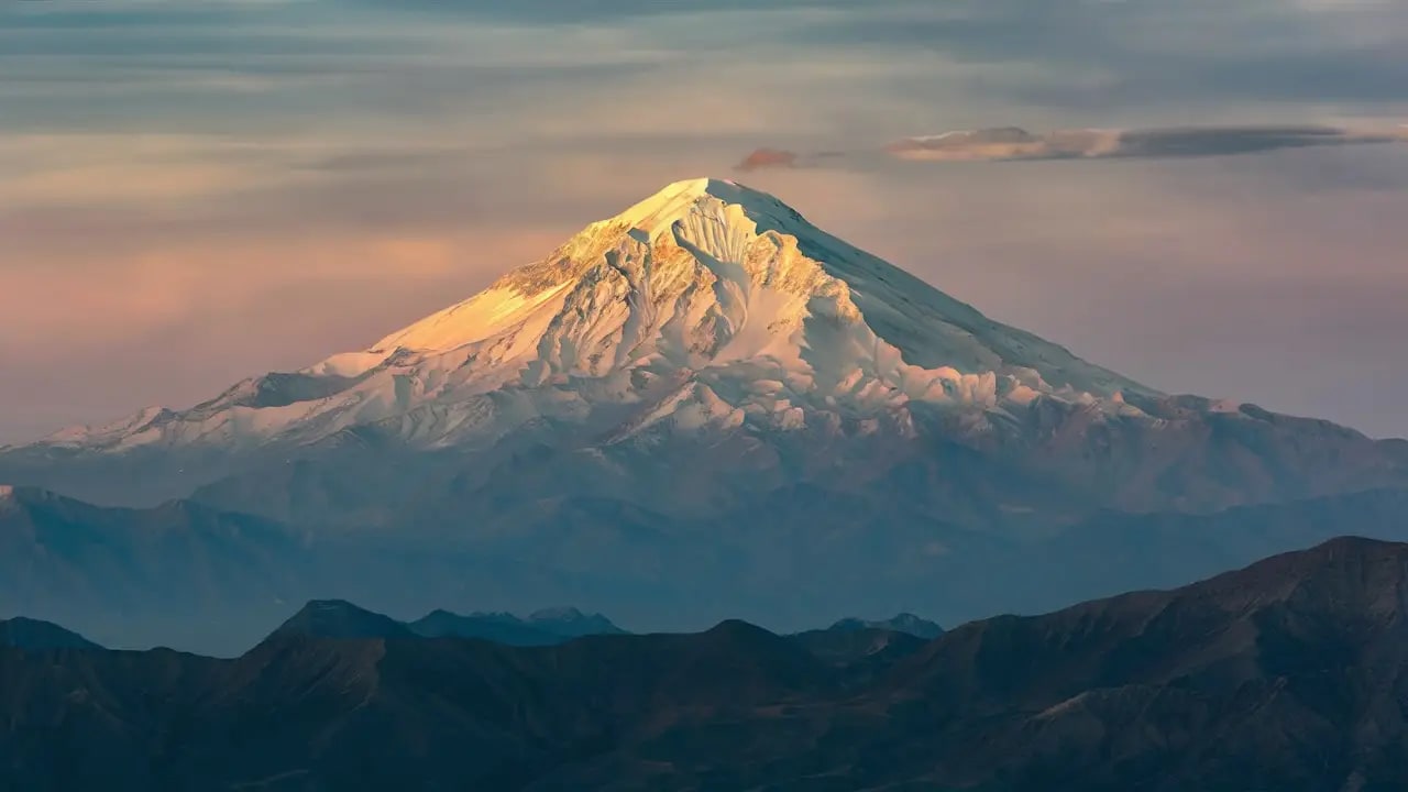 Mount Damavand, the snow-capped conical volcano of northern Iran, rising above green alpine pastures under a clear sky