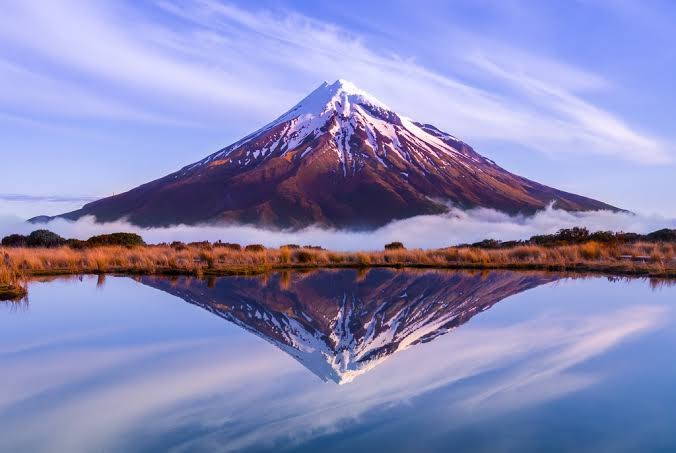 Symmetrical snow-dusted Mount Taranaki volcano rising above native forest on New Zealand's North Island